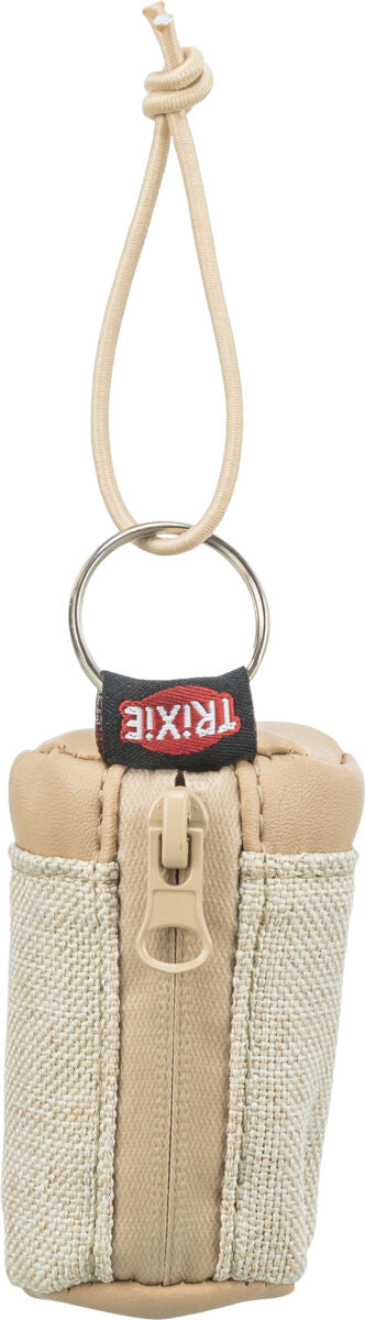 Beigefarbene Tasche mit Reißverschluss, Schlaufe und Ring, Text "TRIXIE" sichtbar.