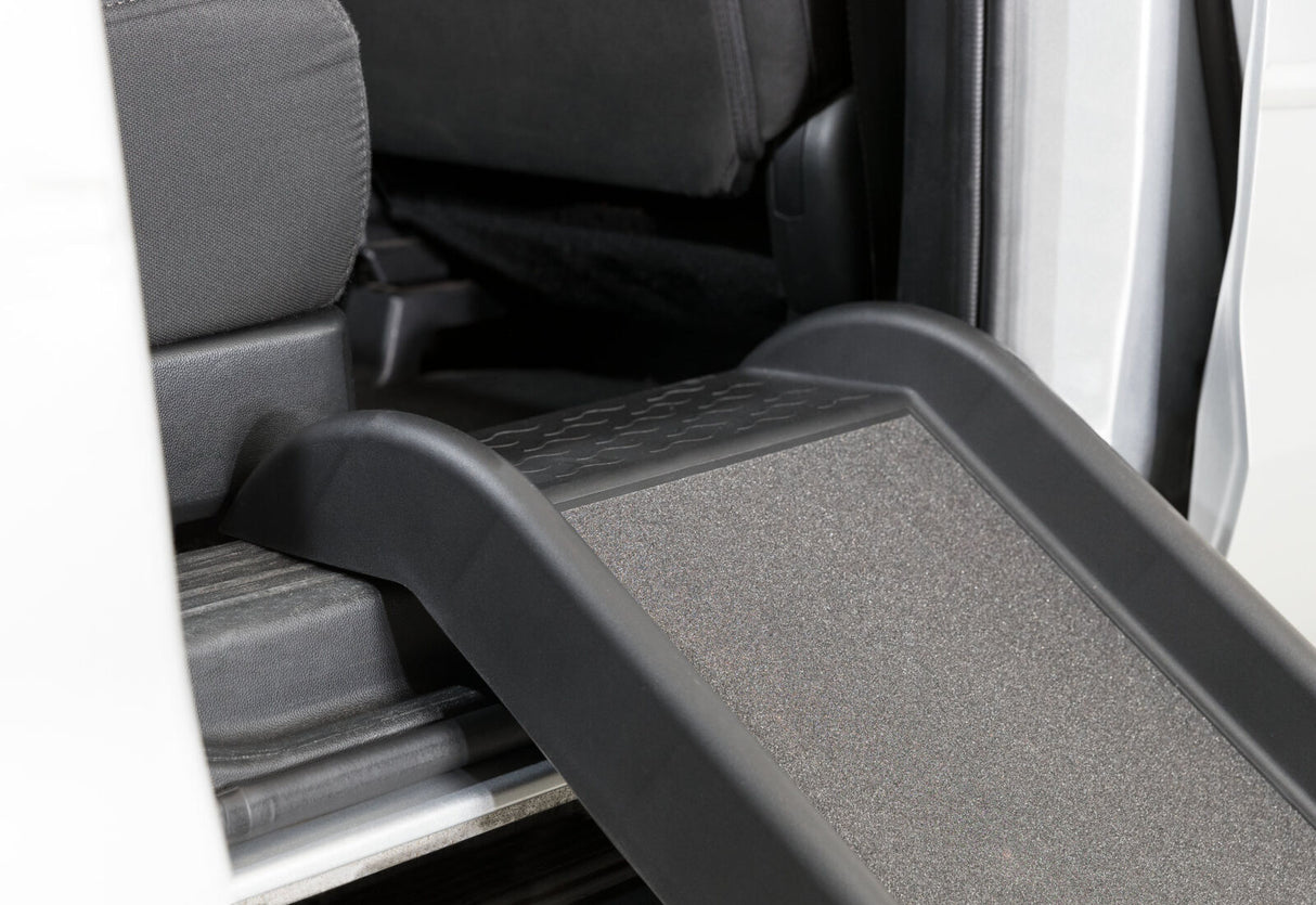 Eine schwarze Rampe führt zu einem Fahrzeuginnenraum mit grauen Sitzen und schwarzem Bodenteppich.
