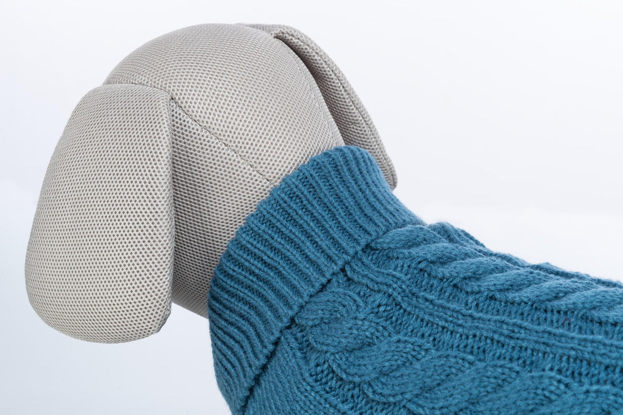 Graues Stofftier mit blauem Strickpullover aus Zopfmuster, weiße Hintergrundfläche.