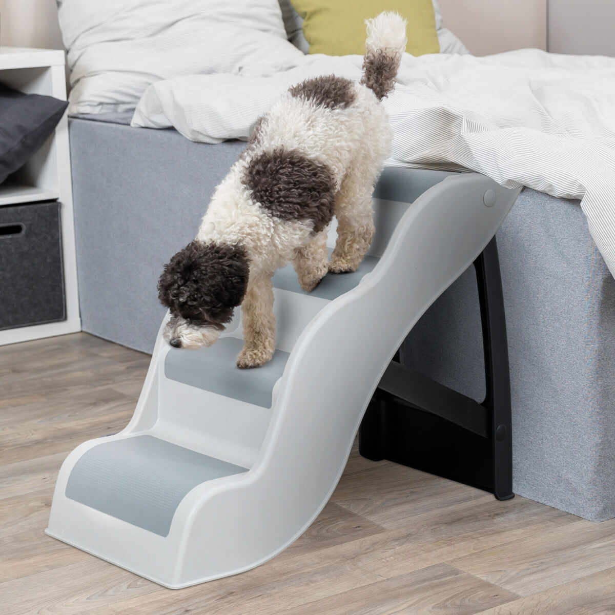 Ein Hund mit lockigem Fell geht eine graue Treppe hinunter, die neben einem Bett steht.