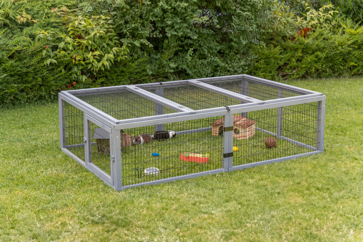 Freigehege aus Metallgitter steht auf einer Wiese, mit Kleintierunterkunft und Spielzeug.