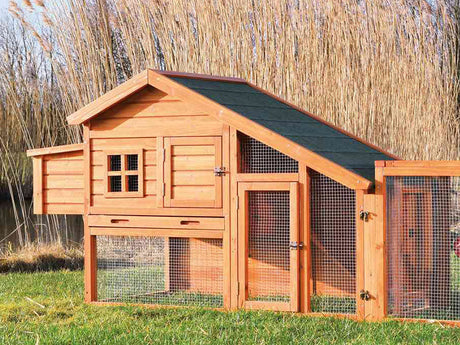 Kleintierstall aus Holz mit Auslaufgehege und grünem Dach auf einer Wiese.