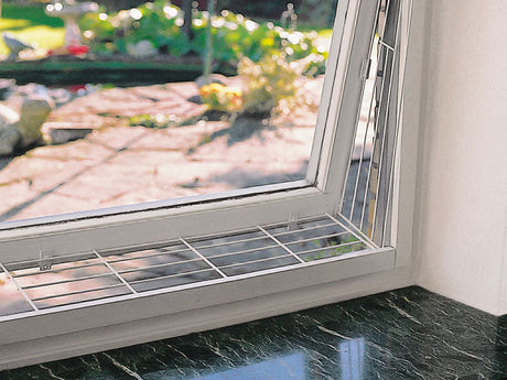 Gekipptes Fenster mit stabilem Schutzgitter vor grünem Garten im Hintergrund