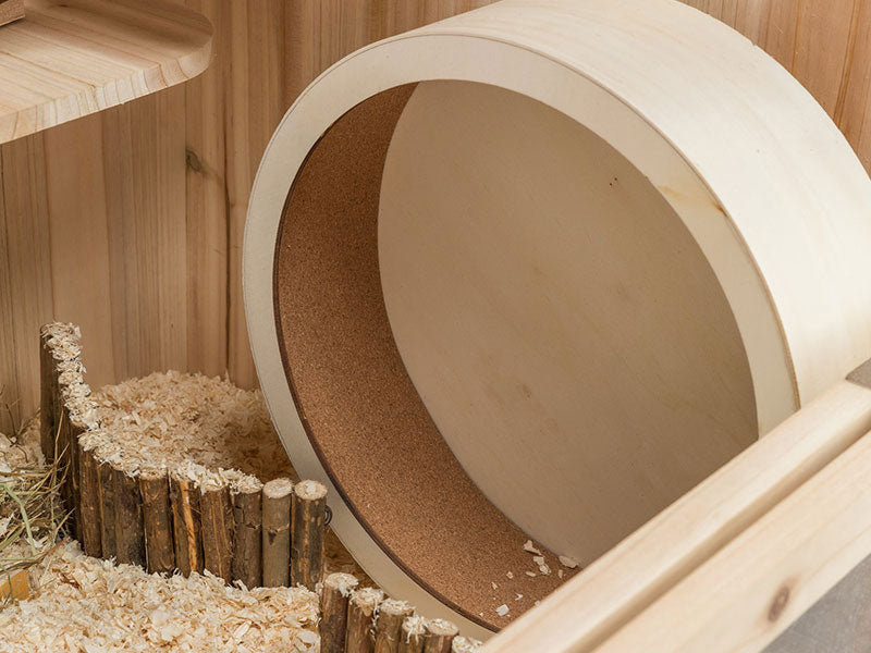 Laufrad aus hellem Holz mit Kork-Innenfläche in einem mit Einstreu ausgestatteten Kleintiergehege.