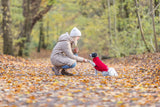 Frau kniet und schüttelt Pfote mit kleinem Hund im roten Pullover auf herbstlichem Waldweg.