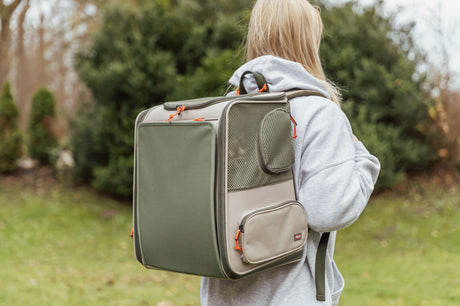 Person trägt einen olivgrünen Transportrucksack mit orangefarbenen Details im Freien.