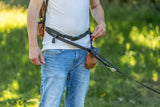 Mann in weißem T-Shirt und blauen Jeans nutzt einen Bauchgurt mit Leine im Grünen.