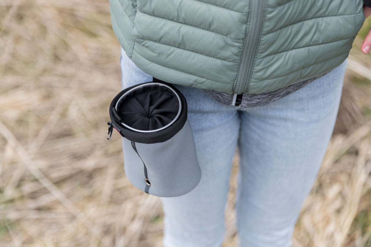 Eine graue Tasche hängt an einer hüfthohen Person in blauer Jeans und grüner Jacke.