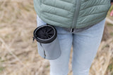 Eine graue Tasche hängt an einer hüfthohen Person in blauer Jeans und grüner Jacke.