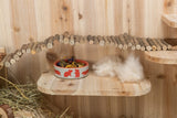 Holzplattform mit Futternapf und Brücke aus Ästen, darüber Holzstreu und Heu.