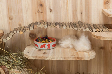 Holzplattform mit Futternapf und Brücke aus Ästen, darüber Holzstreu und Heu.