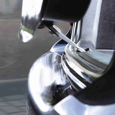 Geöffneter Kofferraum eines Autos mit silbernen Scharnier und glänzender Stoßstange, Detailansicht.