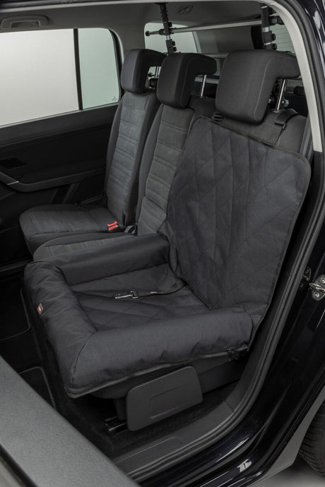 Eine schwarze Hundesitzdecke ist auf dem Rücksitz eines Autos befestigt.
