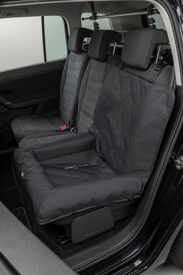 Eine schwarze Hundesitzdecke ist auf dem Rücksitz eines Autos befestigt.
