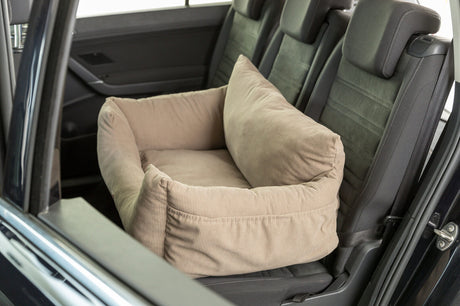 Beiges Hundebett auf dem Rücksitz eines Autos, umgeben von schwarzen Autositzen.