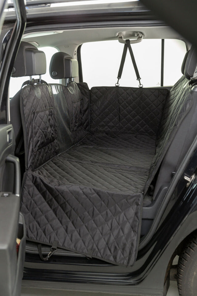 Schwarze, gesteppte Autoschondecke bedeckt die Rückbank und Innenraum eines Autos, Kopfstützen und Sicherheitsgurte sichtbar.