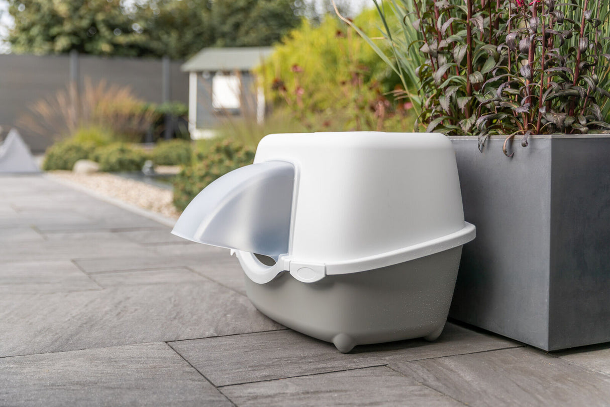 Geschlossene Katzentoilette mit Haube steht auf einer Terrasse neben einem Pflanzkübel.