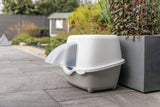 Geschlossene Katzentoilette mit Haube steht auf einer Terrasse neben einem Pflanzkübel.