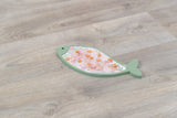 Fischförmige, grüne Unterlage mit bunten Stücken oberhalb auf einem Holzfußboden.