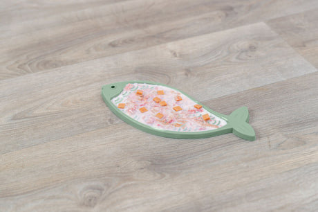 Fischförmige, grüne Unterlage mit bunten Stücken oberhalb auf einem Holzfußboden.