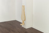 Ein beigefarbenes Kratzbrett in Form einer Katze hängt an einer weißen Wand über einem dunklen Holzboden.