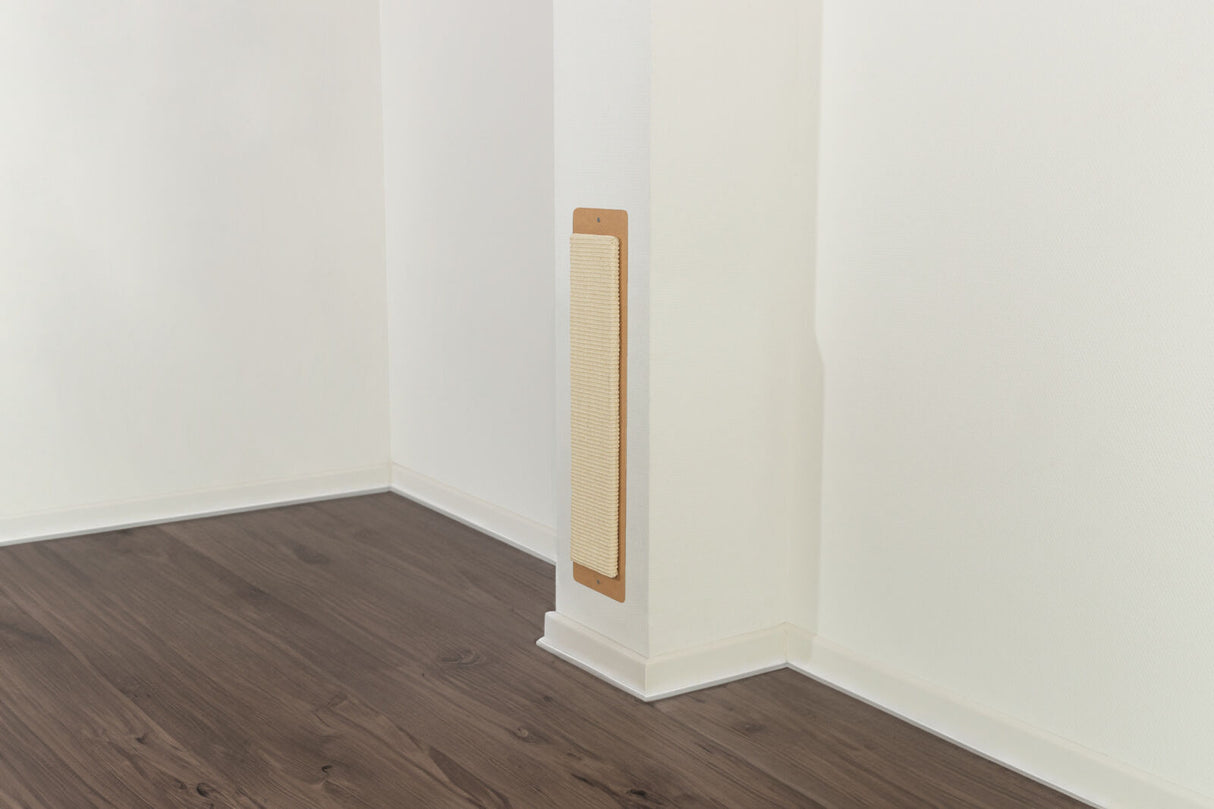 Katzenkratzbrett an einer weißen Wand, befestigt in einer Zimmerecke mit dunklem Holzfußboden.