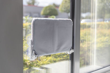 Grauer Fensterliegebrettaufsatz mit Saugnäpfen an Glasscheibe befestigt.