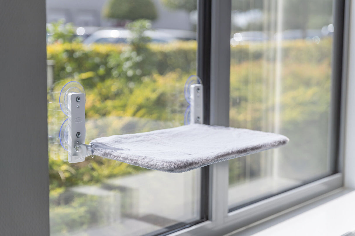 Katzenliege mit grauem Bezug ist an einem Fenster befestigt.