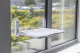 Katzenliege mit grauem Bezug ist an einem Fenster befestigt.