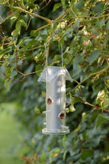Ein silbernes Vogelhaus hängt an einem Ast mit grünen Blättern im Freien.