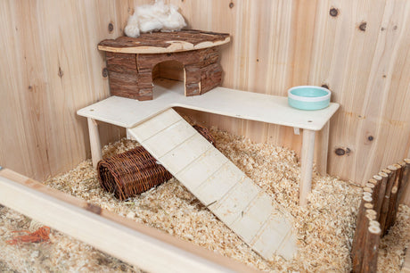 Ein hölzerner Nagerkäfig mit Einstreu, Rampe, kleinem Haus aus Holzplatz und einem blauen Futternapf.
