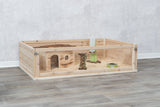 Holzgehege auf Holzfußboden mit Haus, Trinkflasche, Futtertrog und Späne als Einstreu.