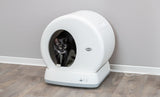 Schwarze Katze in einer runden, weißen Katzentoilette mit Trixie-Logo auf Holzfußboden; elektronisch verbunden.