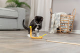 Schwarz-weiße Katze spielt mit gelbem Spielzeug auf Holzboden; Hintergrund mit Korb und Sofa.