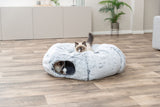 Zwei Katzen sitzen in einem flauschigen grauen Katzenbett auf Holzboden in einem hellen Raum.