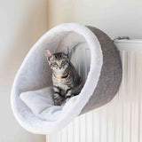 Eine graue Katze sitzt in einer hellgrauen, an der Heizung hängenden Höhle mit weißer Innenpolsterung.