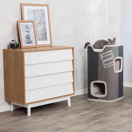 Holzkommode mit weißen Schubladen, darauf Bilderrahmen und eine Kamera, daneben Kratztonne mit Katze, Text "home sweet home".