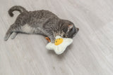 Graue Katze spielt auf hellem Holzboden mit einem Spielzeug in Form eines Spiegeleis.