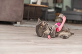Eine graue Katze spielt auf dem Boden mit einem pinken Flamingo-Spielzeug.