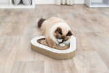 Eine Katze spielt mit einem herzförmigen Kratzbrett aus Pappe auf einem Holzboden.
