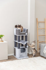 Zwei Katzen spielen auf einem grauen Kratzbaum in einem Wohnzimmer mit Holzboden.
