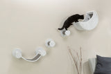 Eine schwarze Katze klettert auf einer an der Wand befestigten Kletterwand aus grauem Stoff mit mehreren Stufen und einer Höhle.