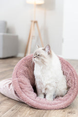 Eine sitzende, flauschige Katze in einer rosa Plüschhöhle auf einem Holzboden im Wohnzimmer.