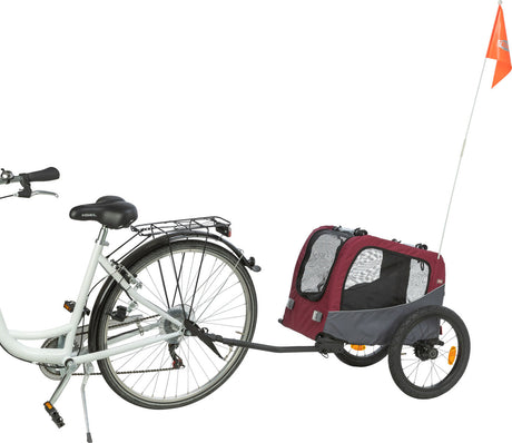 Ein weißes Fahrrad mit einem angehängten, rot-grauen Fahrradanhänger und orangener Fahne.