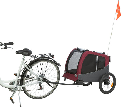Ein Fahrradanhänger in Rot und Schwarz mit Netzeinsätzen und einer orangenen Sicherheitsflagge, die an einem weißen Fahrrad befestigt ist.