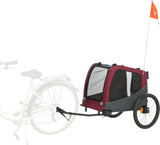 Roter Fahrradanhänger mit zwei Rädern, schwarzem Rahmen und kleinem orangem Wimpel, an Fahrrad angehängt.