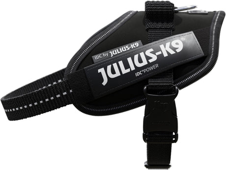 Schwarzes Hundegeschirr mit Aufschriften "JULIUS-K9" und "IDC POWER", reflektierende Streifen, Kunststoffschnalle.