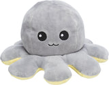 Grauer Plüsch-Oktopus mit lächelndem Gesicht und gelben Akzenten an den Tentakeln auf weißem Hintergrund.
