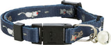 Blaues Halsband mit weißen Katzenmotiven, schwarzem Verschluss und silberner Glocke an einem Ring befestigt.