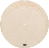 Runde, beige, flauschige Matte mit einem kleinen Loch in der Mitte und einem Etikett am Rand.